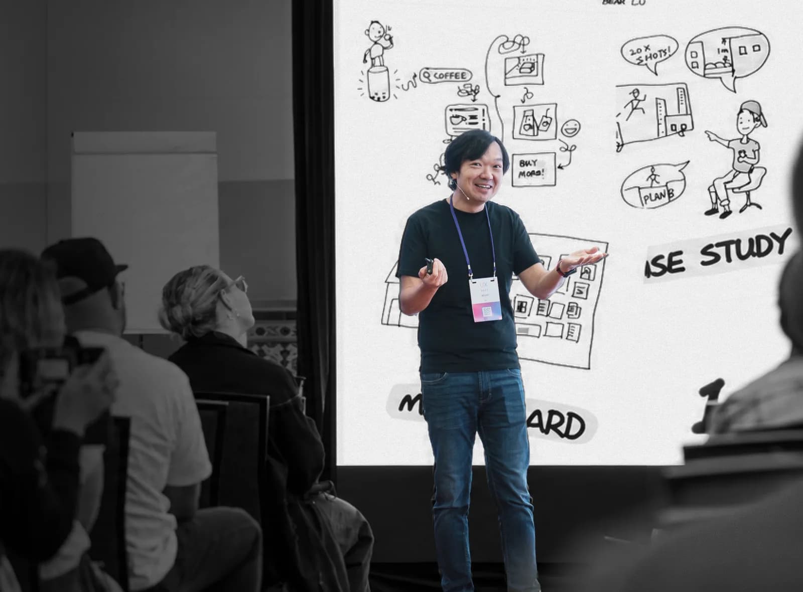 Bear speaking on stage at UX New Zealand, a case study sketch on the screen behind him